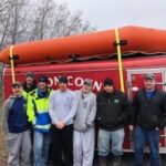 seven man standing in front of a red trailer with an inflatable raft on top